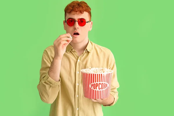 红头发的年轻人吃着绿色背景的爆米花 — 图库照片