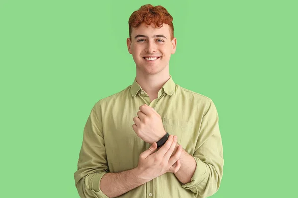 緑の背景にスマートウォッチを持つ若い赤毛の男 — ストック写真