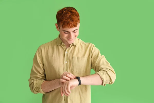 緑の背景でスマートウォッチを見ている若い赤毛の男 — ストック写真