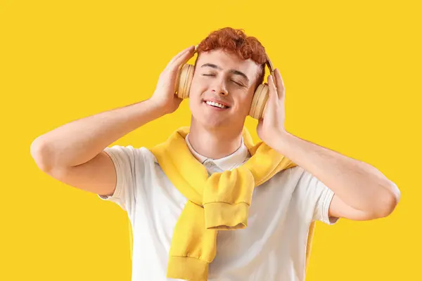 戴着耳机听黄色背景音乐的红头发年轻人 — 图库照片