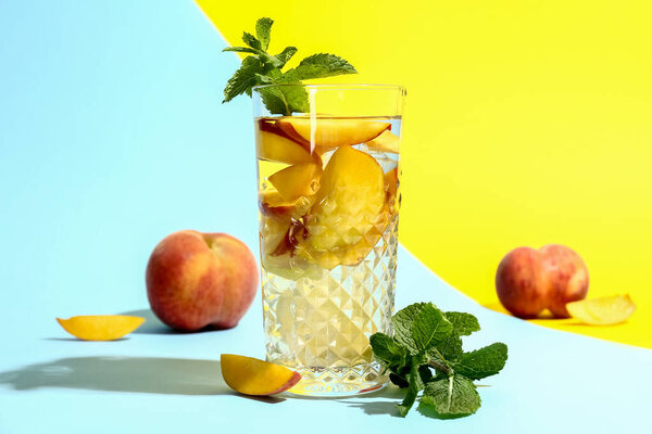 Glass of fresh peach lemonade with mint on colorful background