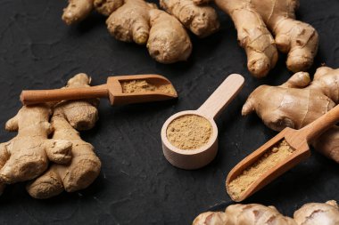 Taze zencefil kökleri, ahşap kepçeler ve siyah arka planda kurutulmuş toz ile kaşık.