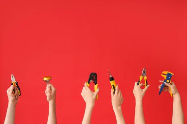 Electrician hands with tools and light bulb on red background