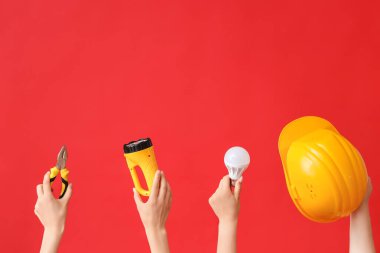 Electrician hands with tools and light bulb on red background