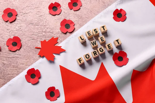Poppy flowers with flag of Canada and text LEST WE FORGET on grunge pink background. Remembrance Day