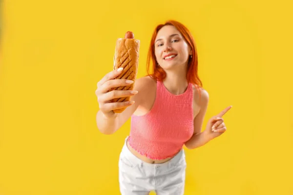 黄色の背景でおいしいフランス語ホットドッグと美しい若い女性 — ストック写真