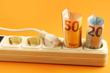 Avro banknotları ve turuncu arka planı olan bir elektrik prizi, yakın plan. Elektrik faturası kavramı