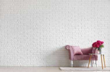 Kahve masasında mum ve beyaz tuğla duvarın yanında kanepe olan kırmızı şakayık vazosu.