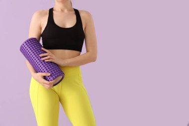 Spor giyimli genç bir kadın ve leylak kaplamalı köpüklü bir silindir.