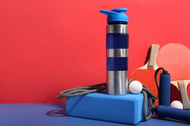 Bir şişe su ve renkli arka planda farklı spor ekipmanları