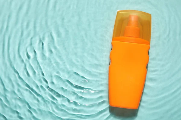 Bottle of sunscreen cream in water on color background