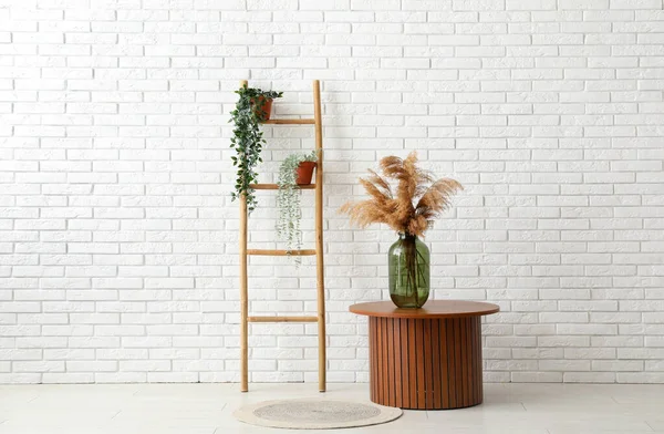 Wooden ladder, table and houseplants near white brick wall in room