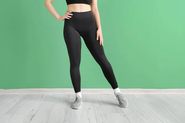 Sporty young woman in leggings near  green wall