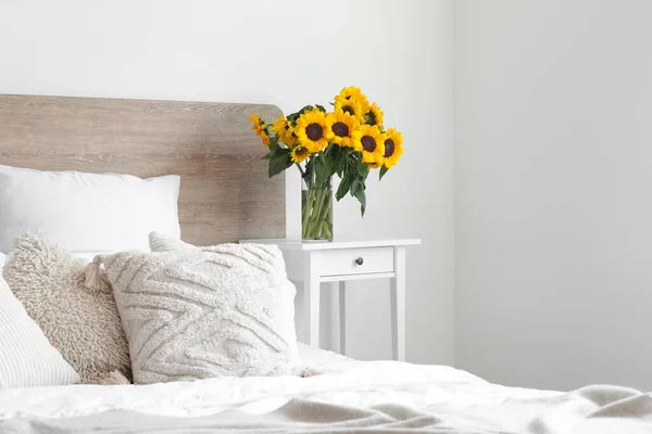 ベッドサイドテーブルの上にひまわりの花束と光の寝室のインテリア — ストック写真