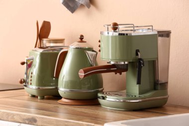 Elektrikli çaydanlık, kahve makinesi ve bej duvarın yanındaki ahşap mutfak tezgahında ekmek kızartma makinesi.