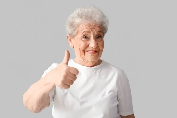 stock image Senior woman showing thumb-up on grey background
