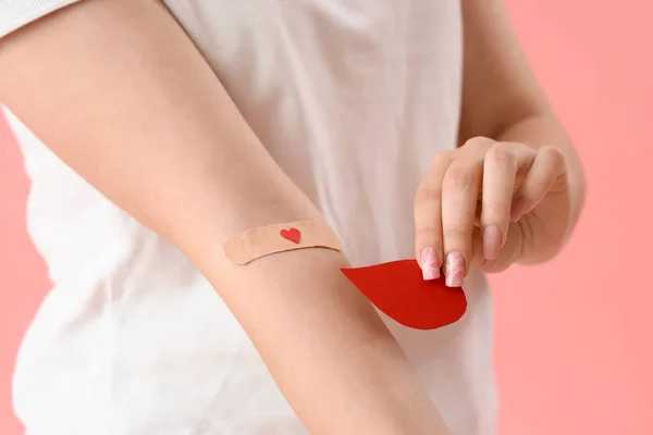 Female donor with applied medical patch and paper blood drop on pink background, closeup