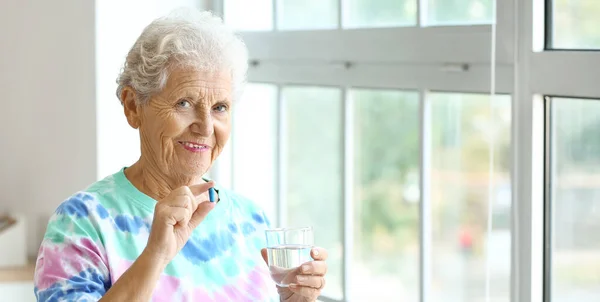 stock image Elderly woman with glass of water taking medicines at home