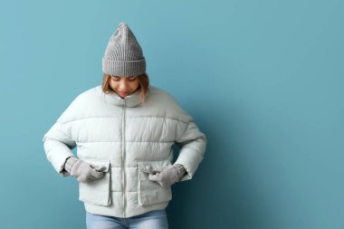 Frozen young woman in winter clothes on blue background