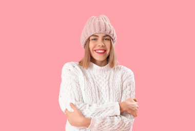Frozen young woman in winter clothes on pink background