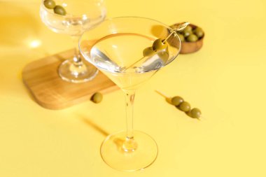 Sarı arka planda zeytinli bir bardak martini.
