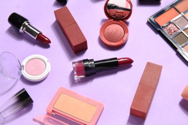 Leylak arka planında ruj lekeleri olan dekoratif kozmetik ürünler.