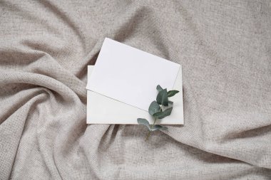 Gri buruşuk masa örtüsünün üzerinde okaliptüs dalı olan boş davetiye kartı