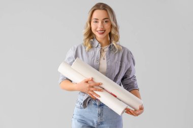 Gri arka planda duvar kağıdı ruloları olan genç bir kadın.