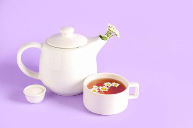 Bir fincan doğal papatya çayı, şeker ve çiçekli bir çaydanlık.