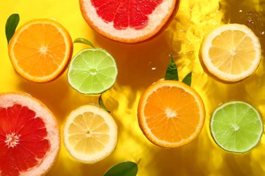 Farklı narenciye dilimleri ve yaprakları sarı arka planda.