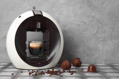 Gri grunge masasında bir fincan espresso, kozalar ve fasulye ile modern kapsül kahve makinesi.