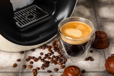 Bir bardak nefis espresso, kapsül kahve makinesi, kapsüller ve fasulyeler gri grunge masasında.