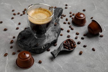 Lezzetli bir fincan espresso, gri grunge masasında fasulye ve kapsüller.
