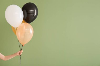 Yeşil arka planda farklı Cadılar Bayramı balonları olan kadın eli
