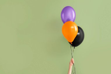 Yeşil arka planda farklı Cadılar Bayramı balonları olan kadın eli