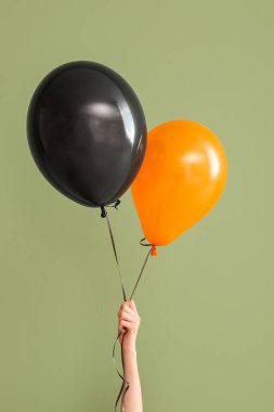 Yeşil arka planda farklı Cadılar Bayramı balonları olan kadın eli