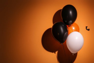 Cadılar Bayramı balonları ve yarasalar turuncu duvarda asılı.