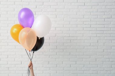 Farklı Cadılar Bayramı balonları olan kadın eli odada hafif tuğla duvarın yanında.