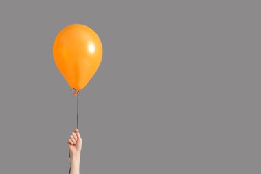 Gri arka planda turuncu Cadılar Bayramı balonu olan bir kadın el.