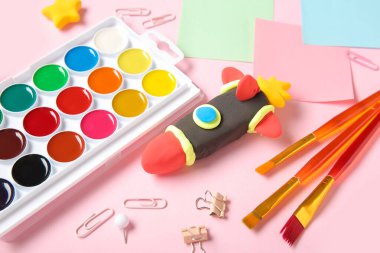 Pembe arka planda farklı kırtasiye malzemeleriyle plastikten yapılmış roket