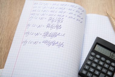 Hesap kitaplarını matematik formülleri ve hesap makinesiyle ahşap masa üzerinde aç, kapat