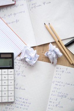 Matematik formüllü metin kitapları, parçalanmış kağıt ve hesap makinesi ahşap masa üzerinde.