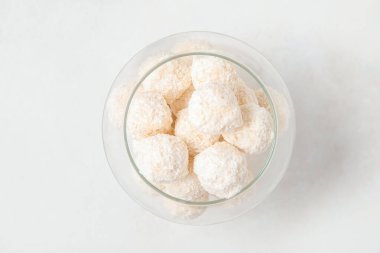 Hindistan cevizi kaplı beyaz çikolata şekerleri cam kasede ışık masasında.