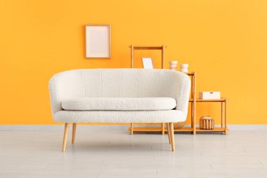 Saf beyaz kanepe ve sarı duvarın yanında çerçeveleri olan raf ünitesi.