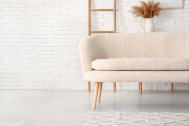 Tuğla duvarın yanında halı olan rahat beyaz kanepe.