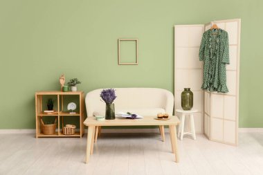 Katlanır ekran, raf ünitesi, kanepe, masa ve güzel lavanta çiçekleri olan şık bir oturma odası.