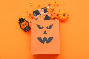 Alışveriş torbası, fener, hediye kutusu ve turuncu arka planda Cadılar Bayramı için lezzetli şekerler.