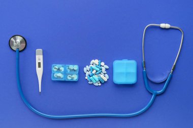 Mavi arkaplanda stetoskop, hap ve dijital termometre