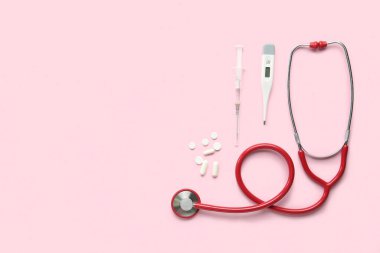 Pembe arka planda tıbbi steteskop, hap, şırınga ve dijital termometre