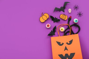 Mor arka planda Cadılar Bayramı için alışveriş torbası, yarasa, örümcek ve lezzetli şekerlerle kompozisyon